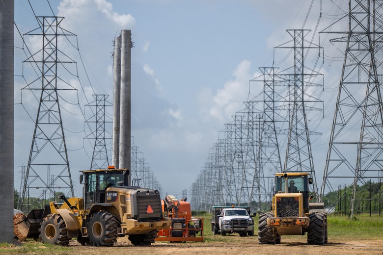 Bulldozers and trucks are seen in front of a series of power lines and a transmission tower.